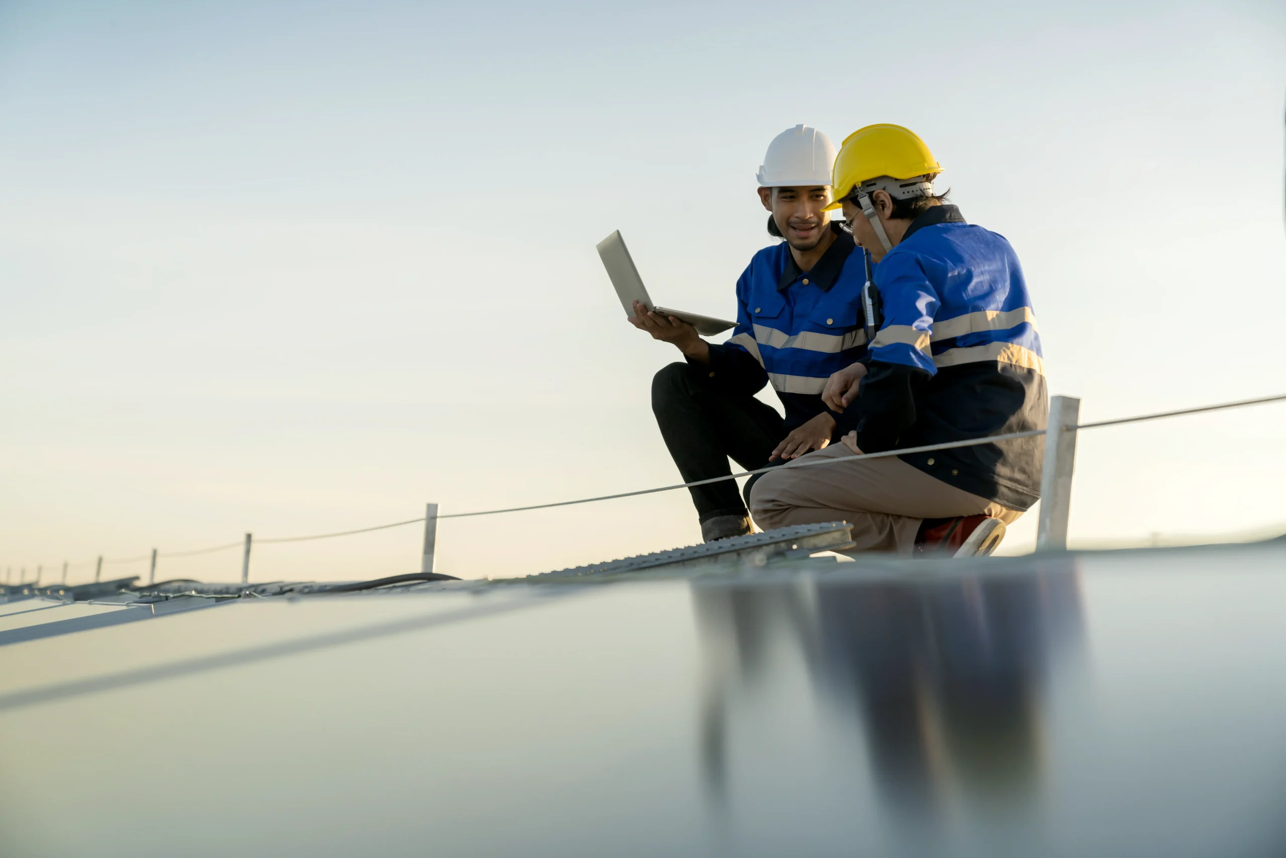 Solar panel engineers using a laptop while inspecting a commercial rooftop installation